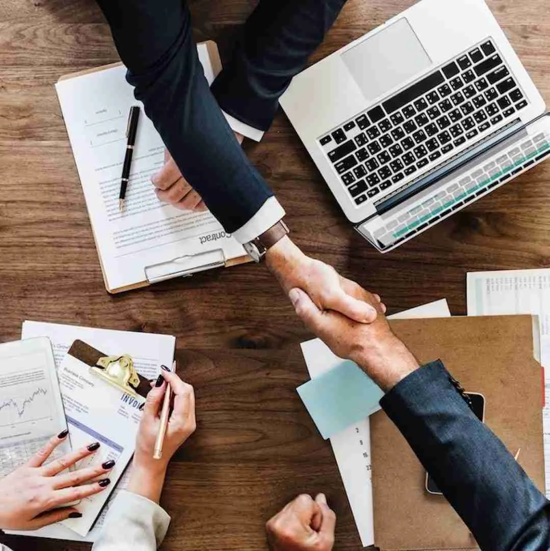 handshake between two business partners over a wooden table with a laptop and documents