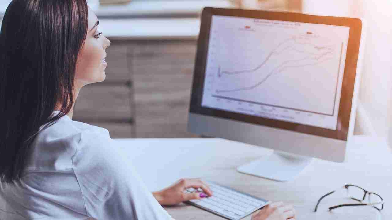 corporate assistant standing a desk looking at a screen with charts