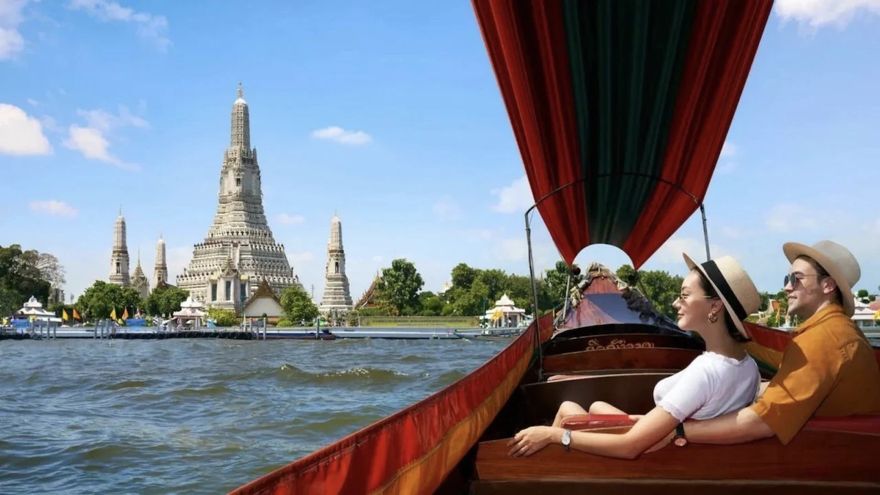 a couple sitting in a private traditional boat on Chao Phraya river in bangkok near a temple