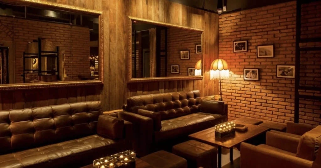 lounge part of whisgars bar in bangkok with large leather sofas mirrors and warm light
